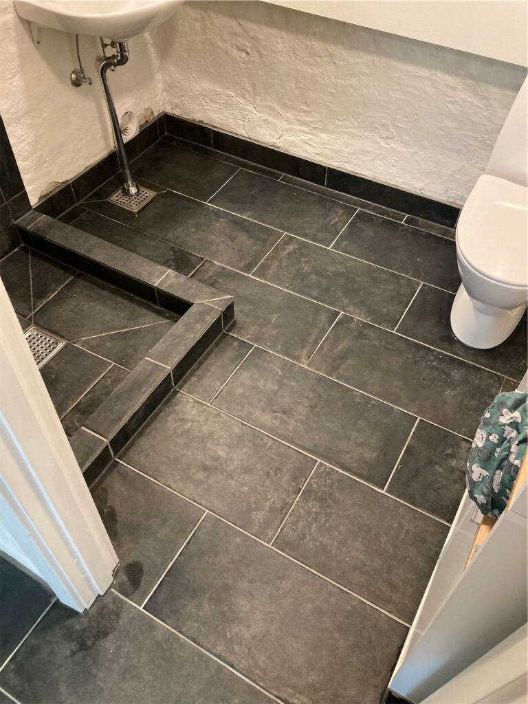 Sort flisebelagt badeværelsesgulv med toilet og vask