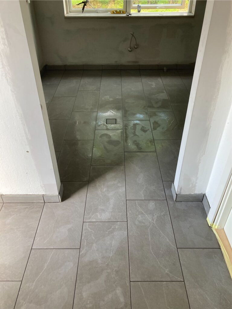 Nyflisebelagt køkkengulv under renovering, vindue i baggrunden.
